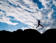 A man leaping from a rock with a beautiful sky behind.